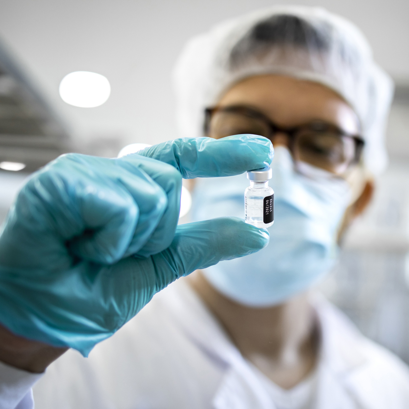 A worker wearing PPE grasps a vial.